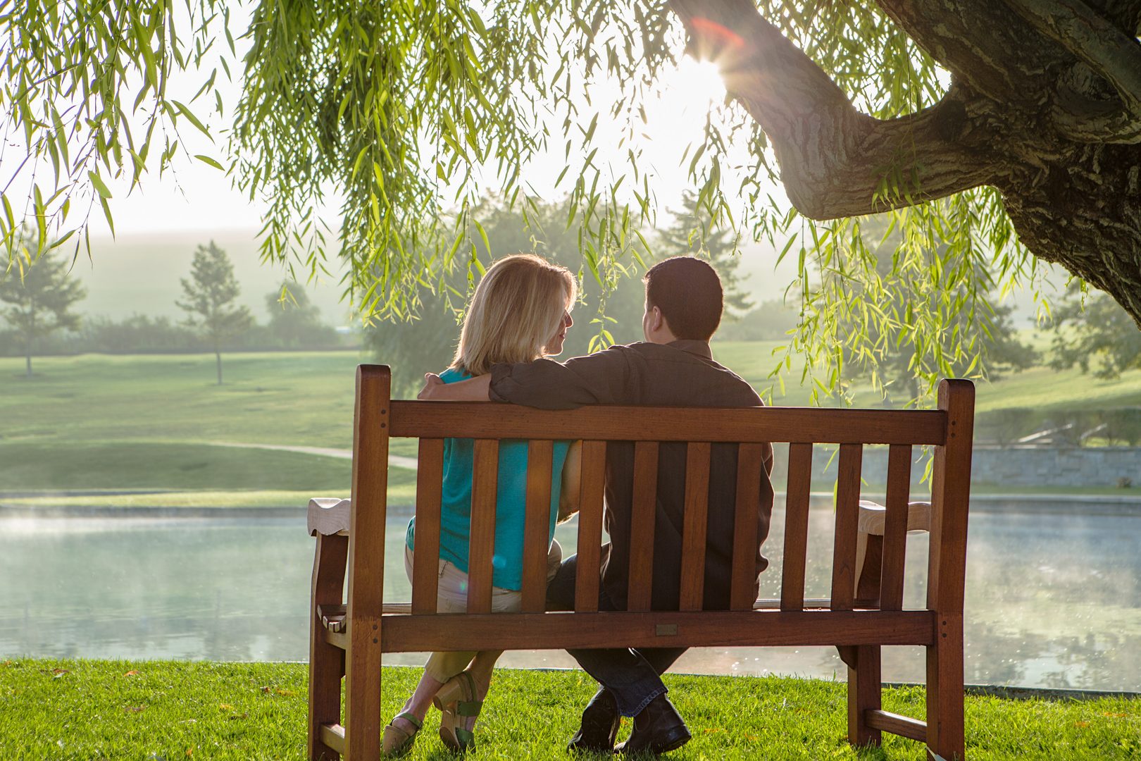 Couple sitting on bench under willow tree